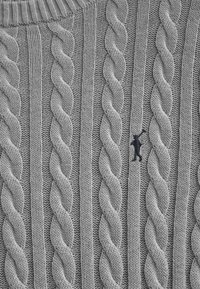 Grauer gestrickter Pullover mit Zopfmuster, der gedrehte Maschen und einen gerippten Kragen aufweist. Kleines schwarzes Logo nahe der Mitte.