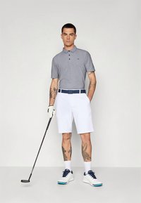 Pilkas polo marškinėlis su dviem sagomis, baltos šortai, mėlynas diržas, balti sportbačiai su mėlynomis detalėmis ir golfo lazda rankoje.