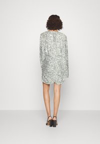 Stříbrná šatna s flitry a dlouhými rukávy, kulatým výstřihem a asymetrickým lemem, doplněná černými sandály na blokovém podpatku.