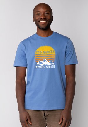 Lichtblauw katoenen t-shirt met een grafische print van een zon en bergen, met de tekst "MEHR WANDERN, WENIGER SORGEN" in wit en geel.