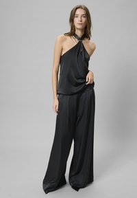 Top halter nero in satin con apertura a forma di chiave e dettaglio annodato al collo, abbinato a pantaloni neri a vita alta e dal taglio morbido.