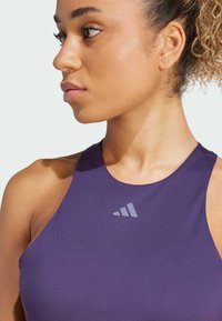 Lilla sports tanktop med høj hals og et logo i lys grå på brystet. Glat tekstur og tætsiddende design.