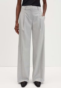 Pantaloni grigi chiari a gamba larga realizzati in un tessuto liscio e tessuto. Presentano pieghe frontali e tasche laterali. Abbinati a delle scarpe nere a punta.
