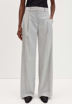 Pantaloni grigi chiari a gamba larga realizzati in un tessuto liscio e tessuto. Presentano pieghe frontali e tasche laterali. Abbinati a delle scarpe nere a punta.