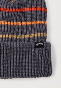 Harmaa neulottu pipo, jossa vaakasuorat raidat oranssina, keltaisena ja punaisena. Pipoon kuuluu taitettu resori, jossa on musta logopläkki toisella puolella.