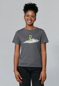 Grijze t-shirt met korte mouwen met een groene cartoonalien op een witte papieren vliegtuig tegen een sterrenhemel. Zachte katoenen stof.