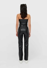 Zwart leren mouwloos topje en bijpassende hoge taillebroek, met een gladde textuur, een strakke pasvorm en minimale details. Witte schoenen zichtbaar.