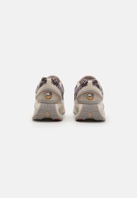 Sneakers with a textured purple and beige upper, featuring a cushioned sole, pull tab, and a circular logo on the heel.