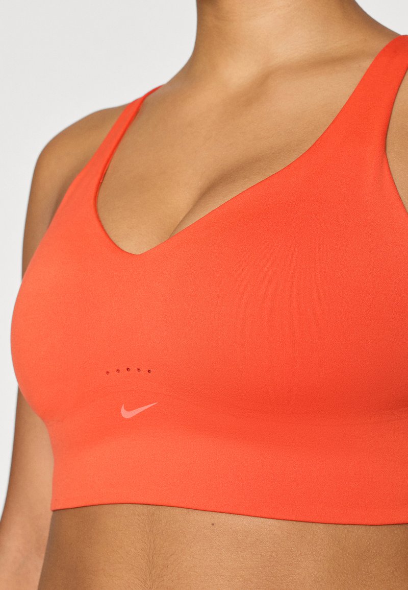 Oranje sportbh met een V-hals ontwerp, gemaakt van gladde stof. Heeft een klein logo en zeven ventilatiegaten in een rij onder de halslijn.