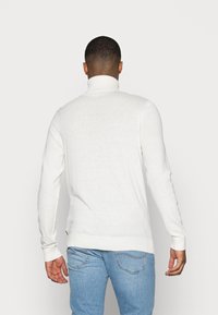 Weißer Rollkragenpullover aus weichem Material mit langen Ärmeln, gerippten Bündchen und Saum. Subtile Textur mit minimalen Designdetails.