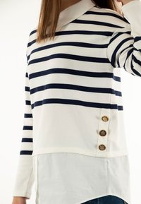 Suéter a rayas en azul marino y blanco. Cuenta con un cuello tipo camisa y tres botones decorativos dorados en el lado. Tejido suave con un aspecto superpuesto.