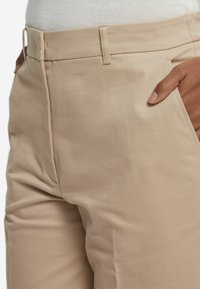 Beiga skräddarsydda byxor i en mjuk bomullsblandning, utrustade med sidofickor, en platt frontdesign och en midjebyxa i normal höjd.