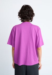Fuksia oversized t-shirt z kratkimi rokavi, okroglo ovratnico in gladko bombažno teksturo. Ima enostaven dizajn brez vidnih vzorcev ali dodatkov.