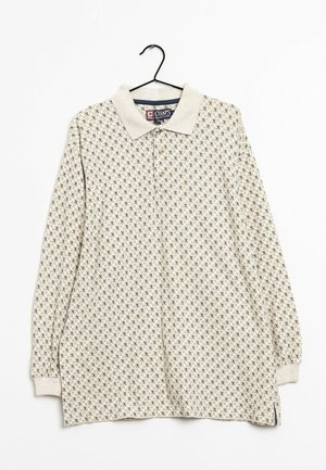 Beige poloshirt met lange mouwen, klein geometrisch patroon in marineblauw en bruin, drieknopsbies en geribbelde boorden, hangend aan een zwarte hanger.