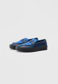 Modré a námořnické slip-on boty s hladkým povrchem, které mají široký pásek a silnou černou gumovou podrážku.