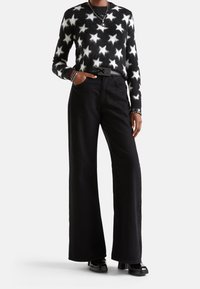 Svart och vit stjärnmönstrad fluffig tröja i kombination med högmidjade svarta vida byxor och glänsande svarta skor, prydd med lager av halsband.