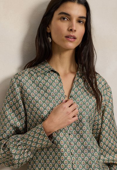 Πράσινο μπλουζάκι με μοτίβο και λουλουδάτη εκτύπωση σε κόκκινο και άσπρο, με γιακά και φουσκωτά μανίκια. Απαλή υφή υφάσματος.