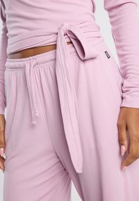 Light pink ribbed loungewear set features a tied waist detail. The top has long sleeves, while the pants have an elastic waistband with drawstrings.