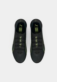Chaussures de sport noires avec une tige texturée, des accents vert fluo et un design courbé. Elles possèdent six lacets et un logo sur la languette.