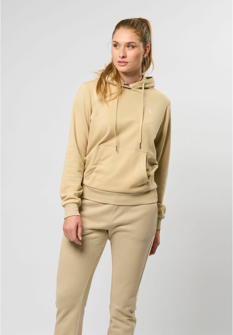 Beige hettegenser med frontlomme og snor, paret med matchende bukser. Myk tekstur, avslappet design, minimal merking.