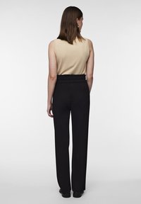 Pantalons larges à côtes noirs avec une taille élastique, associés à un haut sans manches beige. La tenue présente une silhouette élégante et ajustée.