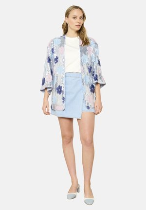 Pailletten kimono in lichtblauw met florale patronen in roze en marineblauw. Gecombineerd met een wit shirt en een denim minirok, aangevuld met twee-kleurige schoenen.