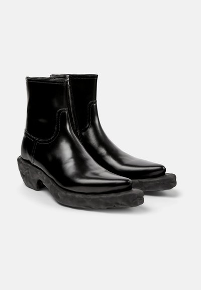 Botines de cuero negro y brillante hasta el tobillo, con puntera afilada, cierre de cremallera y suela de goma negra texturizada y gruesa.