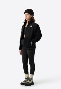 Čierna fleecová bunda so zipsom, doplnená čiernym krátkym topom a legínami. Čierne a krémové turistické topánky. Čierna zapletená čelenka.