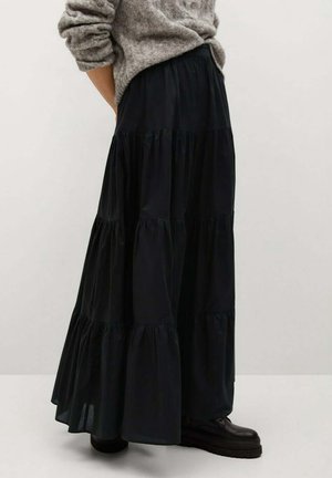 Sort flæset maxi-nederdel lavet af letvægtsstof med en flydende silhuet og detaljer med rynkede sømme. Kombineret med kraftige sorte støvler.