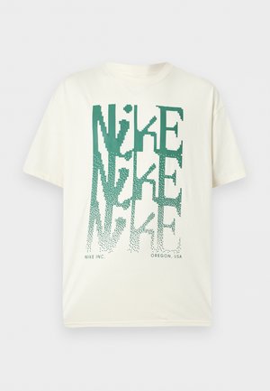 Λευκό T-shirt με κοντά μανίκια με μεγάλο πράσινο παραμορφωμένο κείμενο «NIKE» στοιβαγμένο κατακόρυφα και μικρό κείμενο «NIKE INC. OREGON, USA» στο κάτω μέρος.