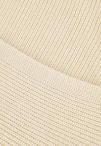 Nahaufnahme von beige geripptem Strickstoff mit einer gefalteten Kante, die zwei verschiedene Strickmuster und Texturen zeigt.