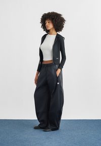 Fekete cipzáras kapucnis pulóver kapucnival és logóval, laza fekete nadrággal, oldalán zsebekkel és fehér részletekkel. Egyszerű fehér, rövidített top.