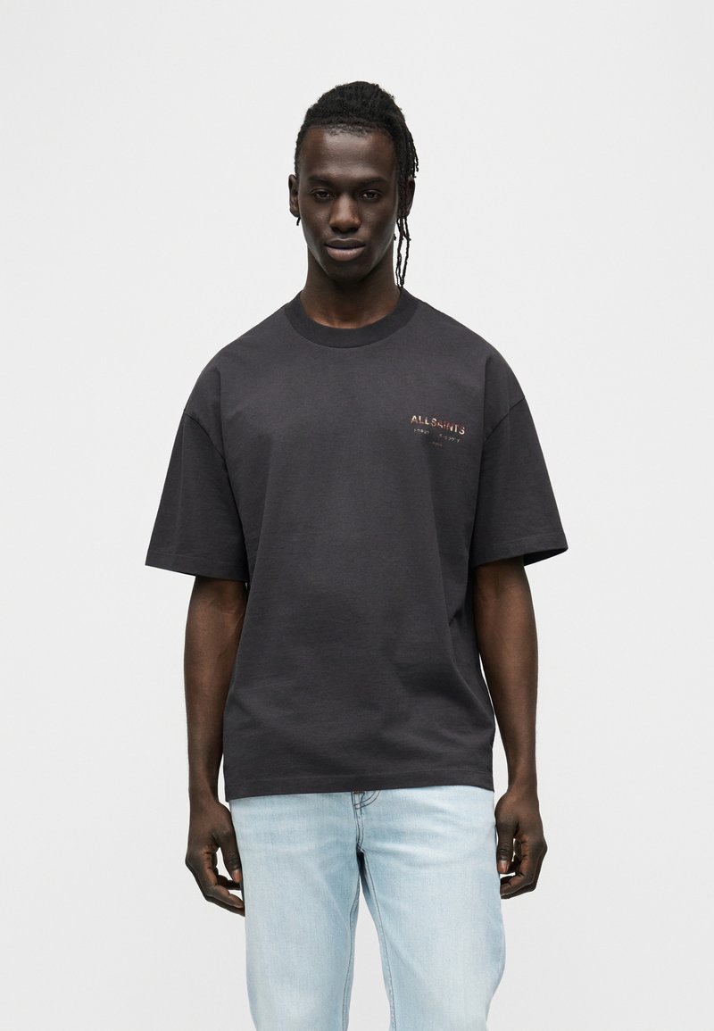 Μαύρο βαμβακερό t-shirt με άνετη εφαρμογή, κοντά μανίκια και μικρή λεπτομέρεια λογότυπου στο στήθος. Συνδυάζεται με ανοιχτόχρωμο τζιν παντελόνι.