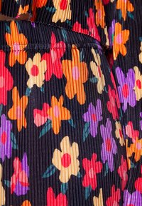 Czarna plisowana tkanina z jasnym wzorem kwiatowym w kolorach pomarańczowym, czerwonym, fioletowym i kremowym, z zielonymi liśćmi.