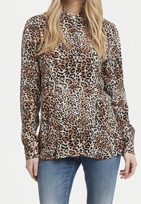 Blusa a maniche lunghe con stampa leopardata in tonalità di marrone e nero, caratterizzata da un collo alto e una vestibilità comoda, abbinata a jeans azzurri.