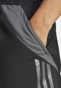 Zwarte sportbroek met grijze accenten, voorzien van een ritszak en drie reflecterende strepen aan de zijkant voor zichtbaarheid.