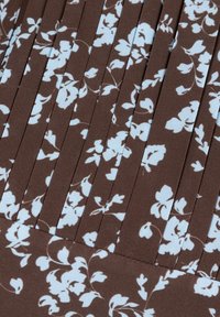 Bruin geplisseerde stof met een bloemenpatroon in lichtblauw, met zichtbare textuur en ruim geplaatste verticale lijnen die een gestructureerd uiterlijk creëren.