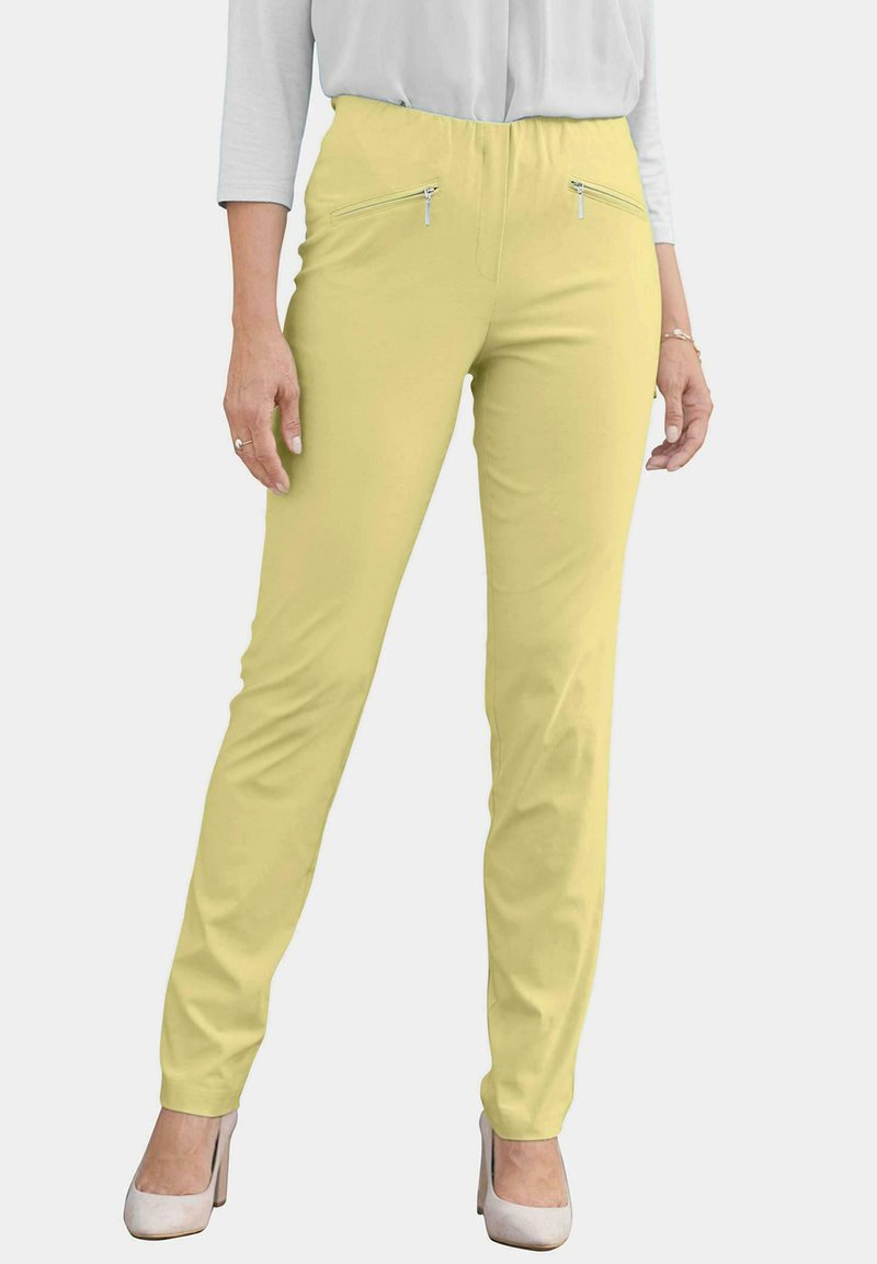 Lichtgele broek met elastische taille, twee voorzakken met rits en een slim fit. Gepaard met een grijze top en witte hakken.
