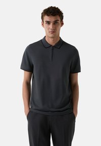 Tmavě šedé polo tričko s límcem na zip a krátkými rukávy. Vyrobeno z hladkého materiálu s přiléhavým střihem. Nosit s černými kalhotami.