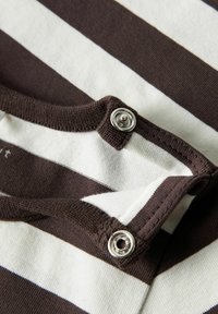 Haut en coton rayé marron et blanc avec un col rond, doté de boutons-pression en argent au col pour la fermeture. Texture douce.