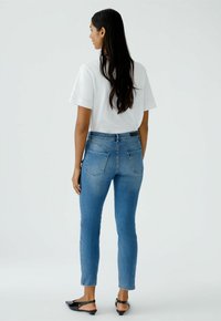 Blauwe denim skinny jeans met een hoge taille, achterzakken en een gladde textuur, gecombineerd met een wit T-shirt en zwarte platte schoenen.