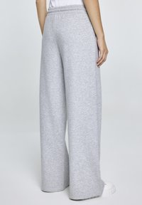 Grijze, wijde sweatpants met een elastische tailleband, zachte textuur en een relaxed fit, gecombineerd met witte schoenen.