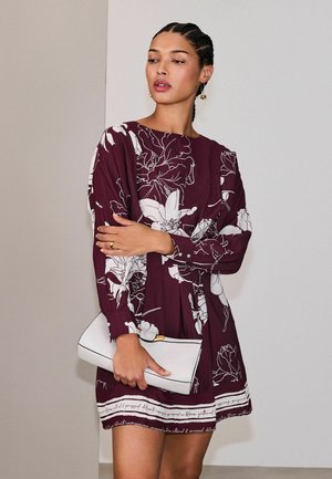 Vīnogu krāsas ziedu kleita ar garām piedurknēm un baltām detaļām, kopā ar baltu somiņu. Kroku dizains ar redzamām pogu detaļām.