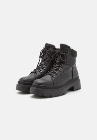 Bottines noires en cuir avec un col en tricot texturé, un laçage à l'avant, un bout rond et une semelle épaisse avec un motif strié.