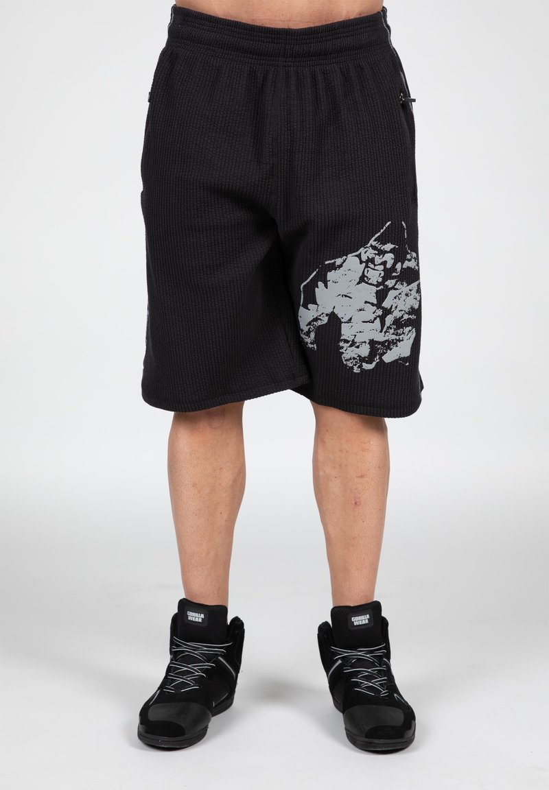 Zwarte sportbroek met een gestructureerd oppervlak, voorzien van een grote grijze opdruk aan de zijkant en een elastische tailleband. Strakke, schuin afgewerkte zoom.