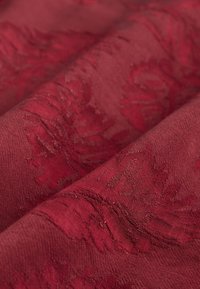 Texturált bordó szövet bonyolult virágmintákkal, sima felülettel és rétegezett redőkkel, amelyek mélységet és részletgazdagságot mutatnak.