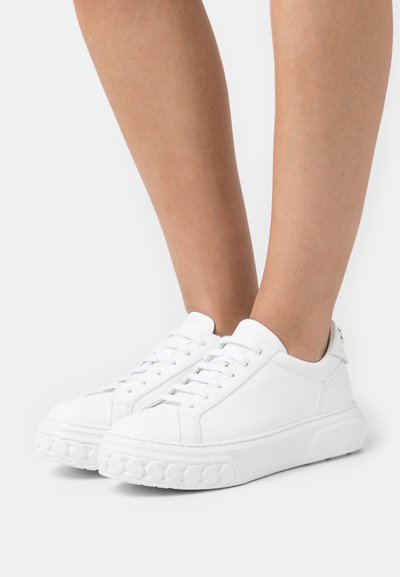 Baskets blanches en cuir avec un bout rond, fermées par des lacets à l'avant, semelle texturée avec un motif de chaîne et un col rembourré.