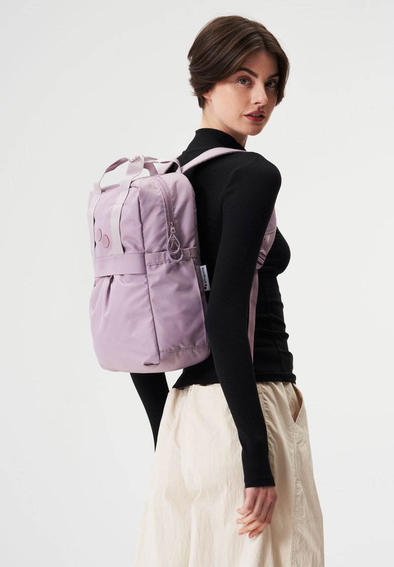 Lila Nylon-Rucksack mit doppelten Obergriffen, verstellbaren Trägern und dezenten kreisförmigen Akzenten. Glatte Textur mit Detail auf der Vorderseite.