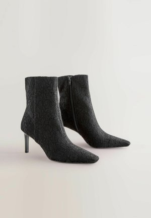 Sorte spidse ankelstøvler i lace med stiletto-hæle. Har en lynlås i siden og struktureret stof med blomsterprint.