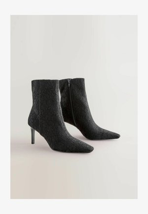 Melnas mežģīņu potīšu zābaki ar norādītiem pirkstiem un stiletto papēdi. Iespējas ir sānu rāvējslēdzis un teksturēts audums ar zieda rakstiem.